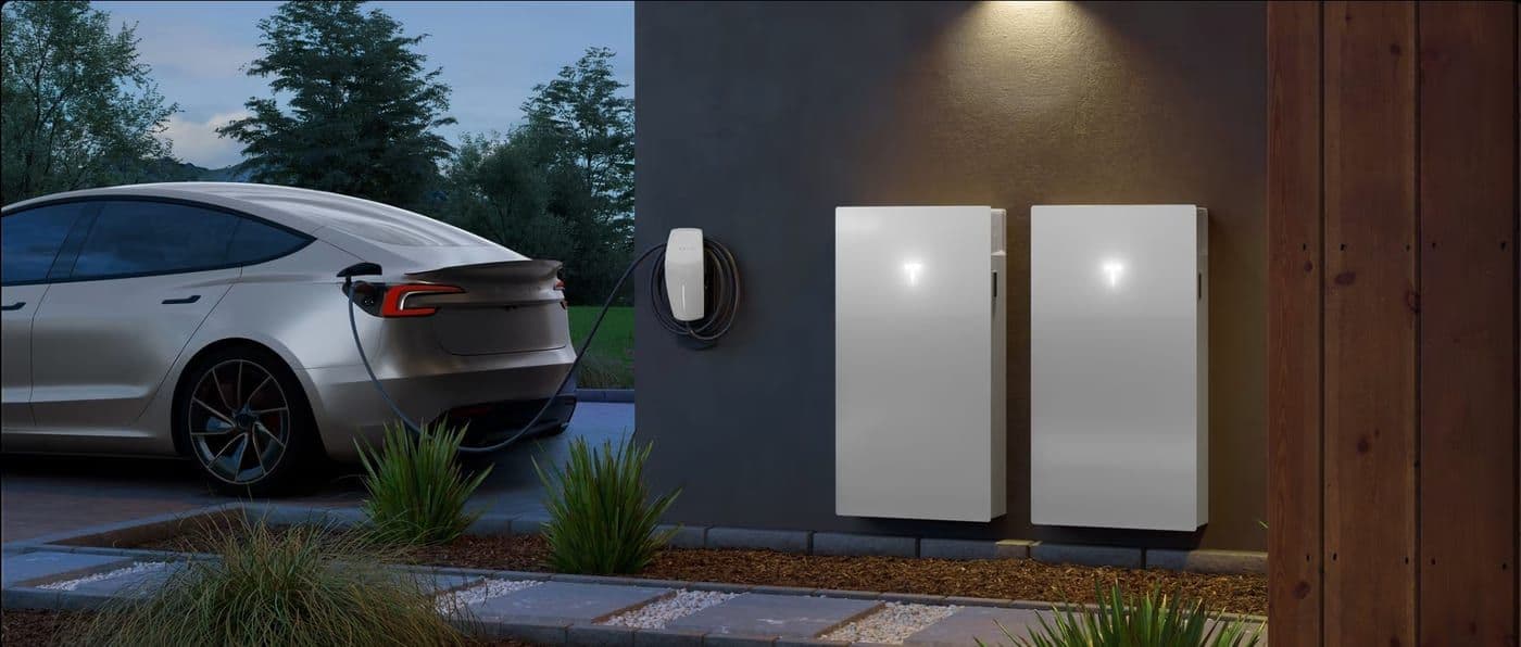 Tesla vehicle charging next to two Powerwall battery units mounted on garage wall