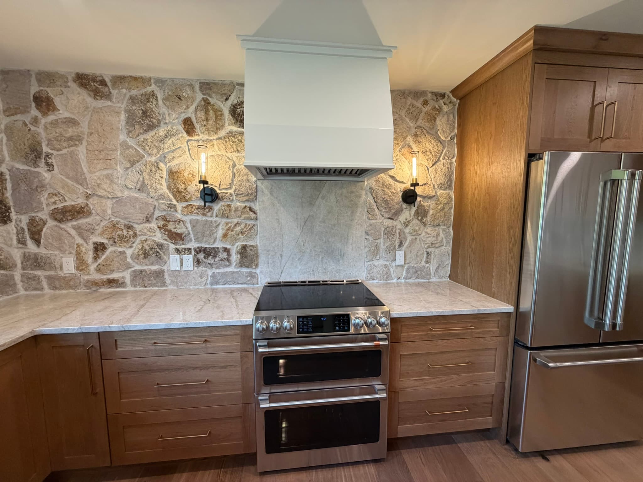 Range and stone hood with stainless appliances against the fieldstone wall