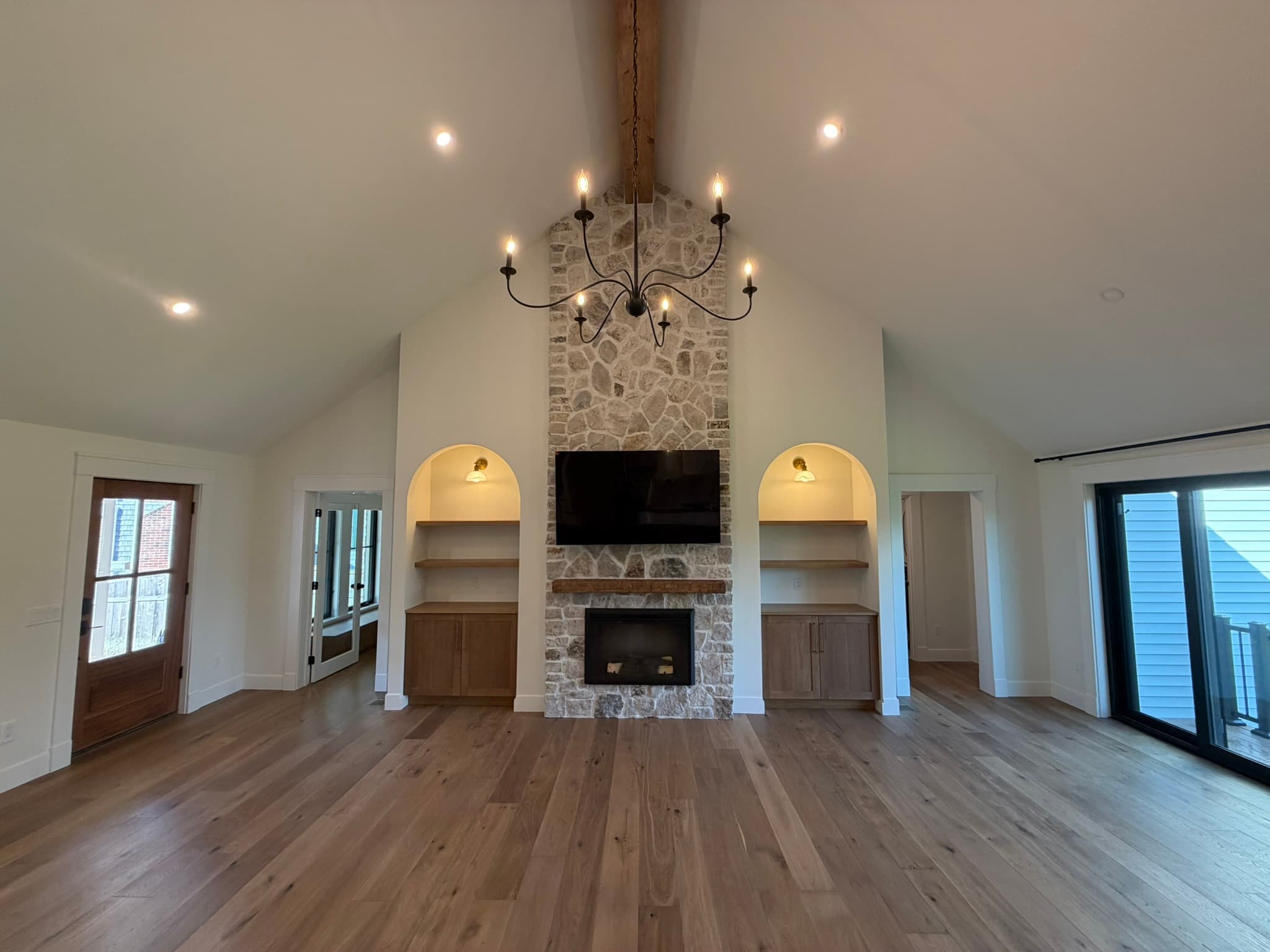 Great room with a floor-to-ceiling stone fireplace (electric — no flue, no combustion), arched built-ins, and a vaulted ceiling
