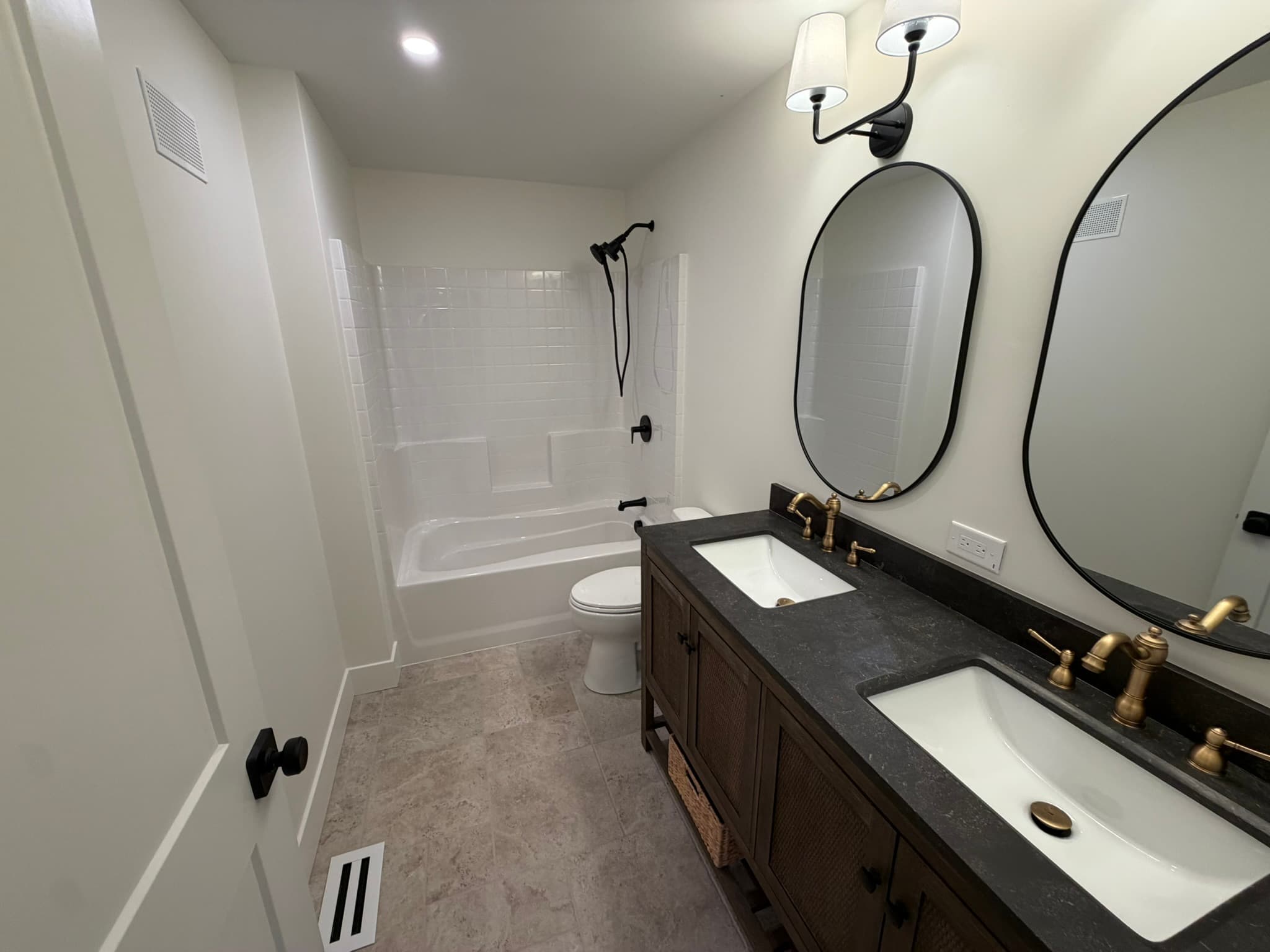Secondary bath with a double vanity, oval mirrors, and brushed-gold fixtures