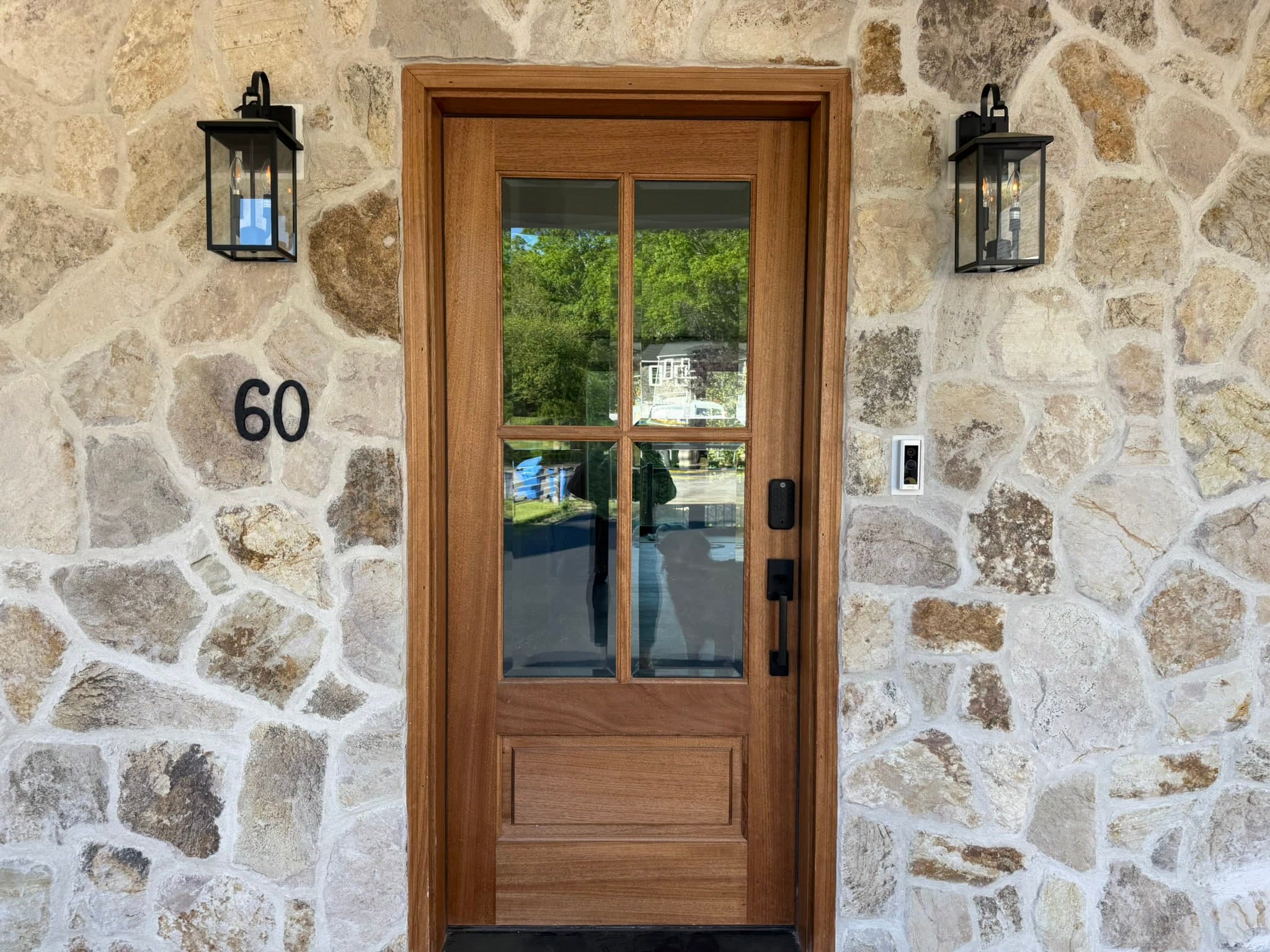 Front-door detail — glazed mahogany door and carriage sconces set in fieldstone, house number 60