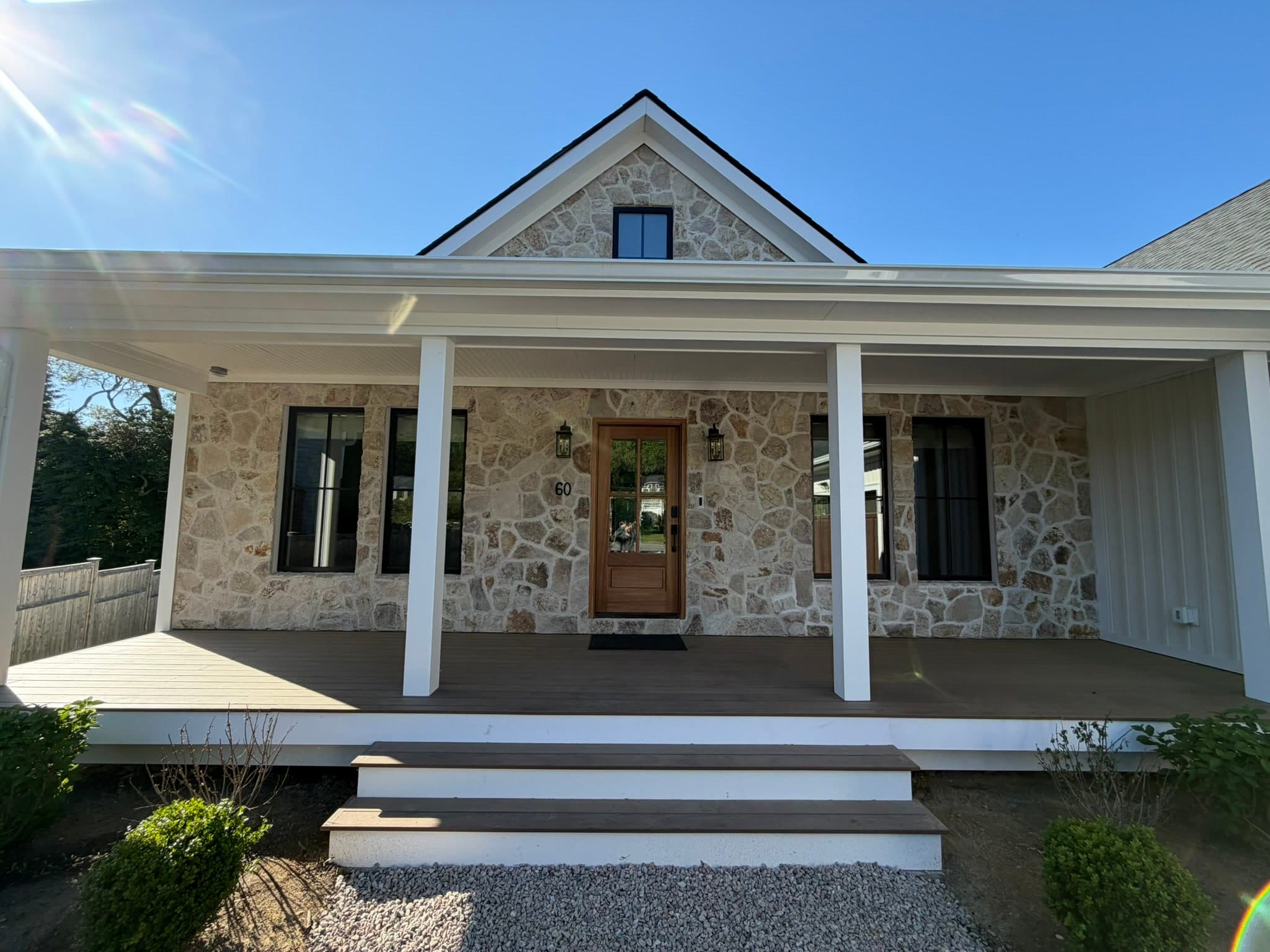 Covered stone front porch with white columns and a mahogany front door